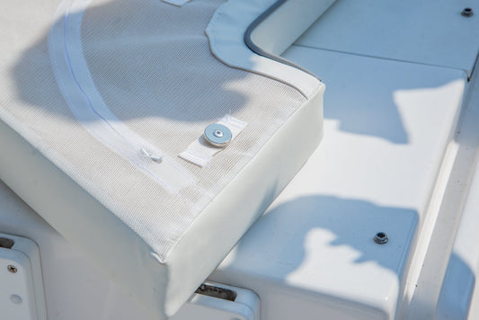 White boat seat cushion with a metal snap fastener, resting on a white fiberglass surface.
